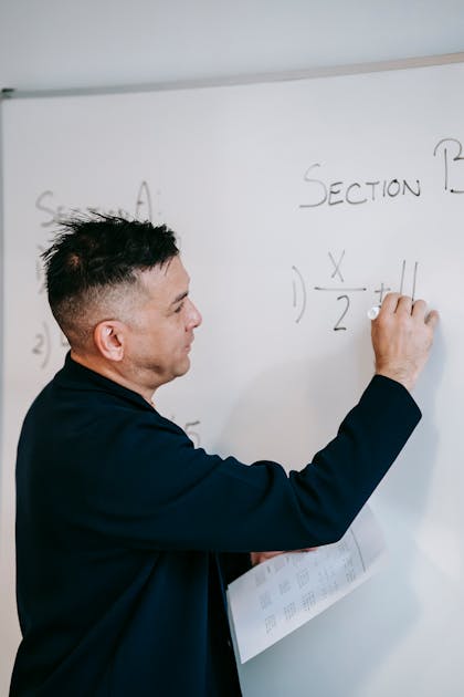 Math teacher writing equations on whiteboard with students in classroom
